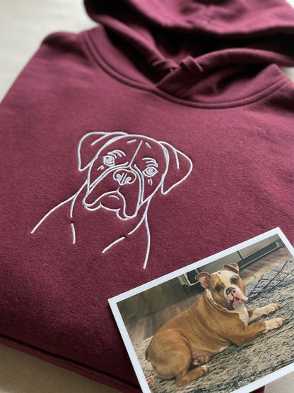 A pet portrait embroidered in white thread on a maroon hoodie, with the owner's own photo of the dog printed and lying beside it