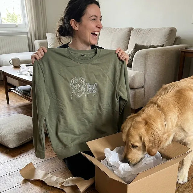 A woman laughing as she unfolds an embroidered sweatshirt from a gift box