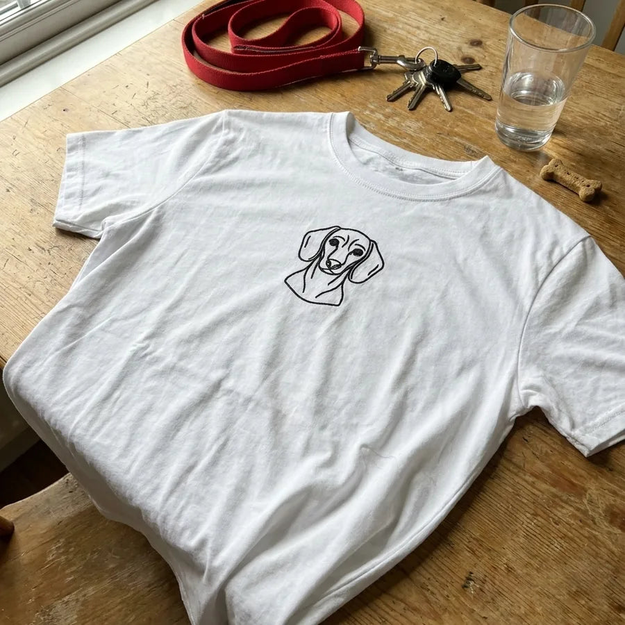 A white t-shirt with an embroidered dachshund, laid on a kitchen table beside a lead and keys